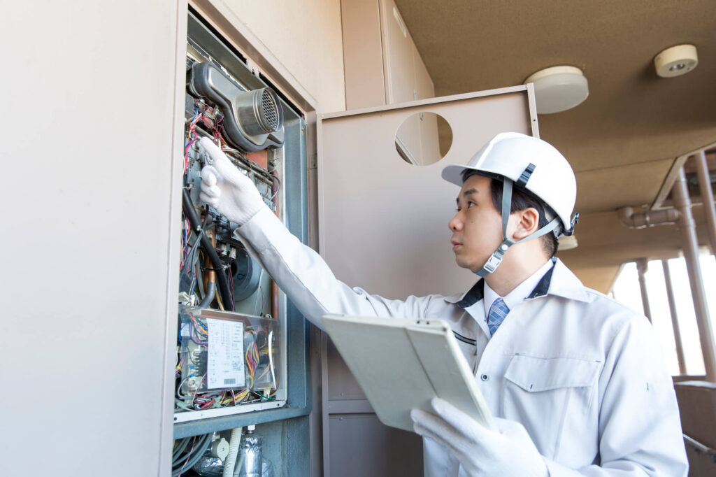 集合住宅のパイプスペース内にある給湯器を点検する作業員