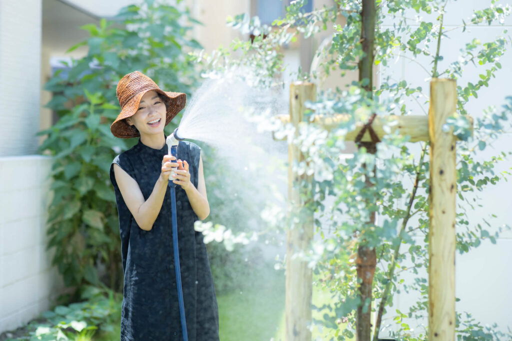 立水栓からホースを伸ばし、庭の植物に水やりをする女性